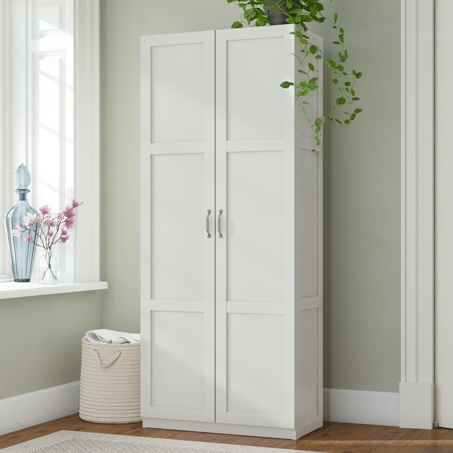 White wardrobe against a light green wall with a window and decorative items.