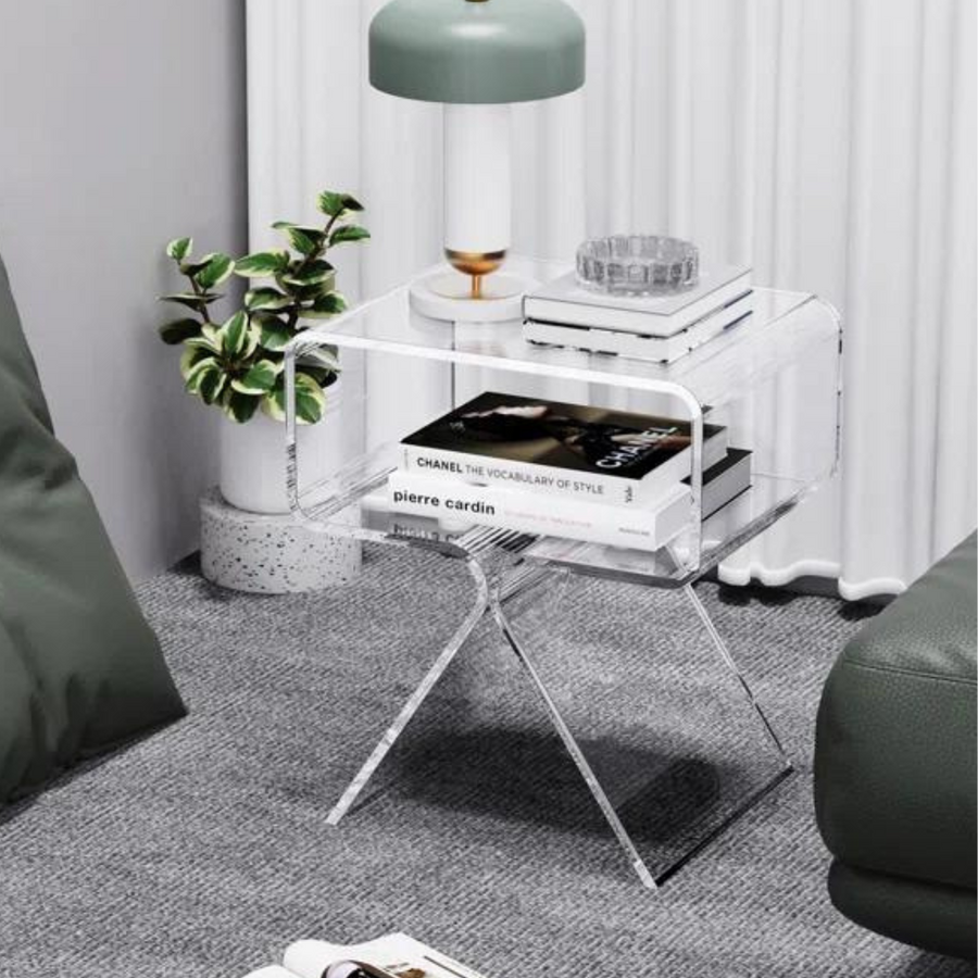 A clear acrylic end table with a minimalist design, featuring a smooth top and a tripod base, displayed in a room setting with decorative items and plants on top.