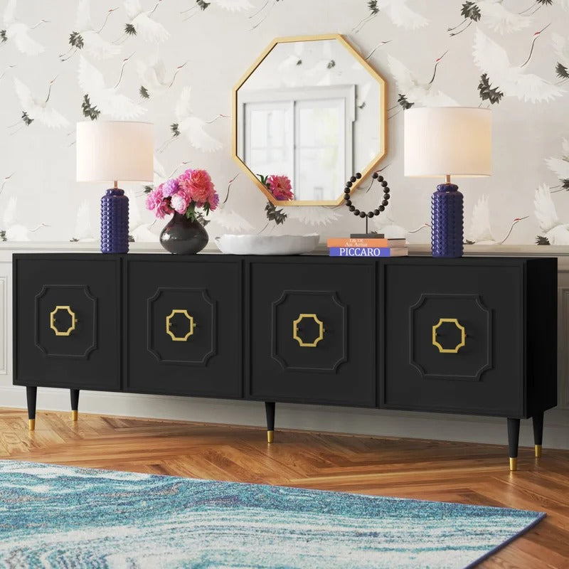A black sideboard and cabinet with gold handles and a mirrored back, placed in a room with a floral arrangement and decorative items on top.
