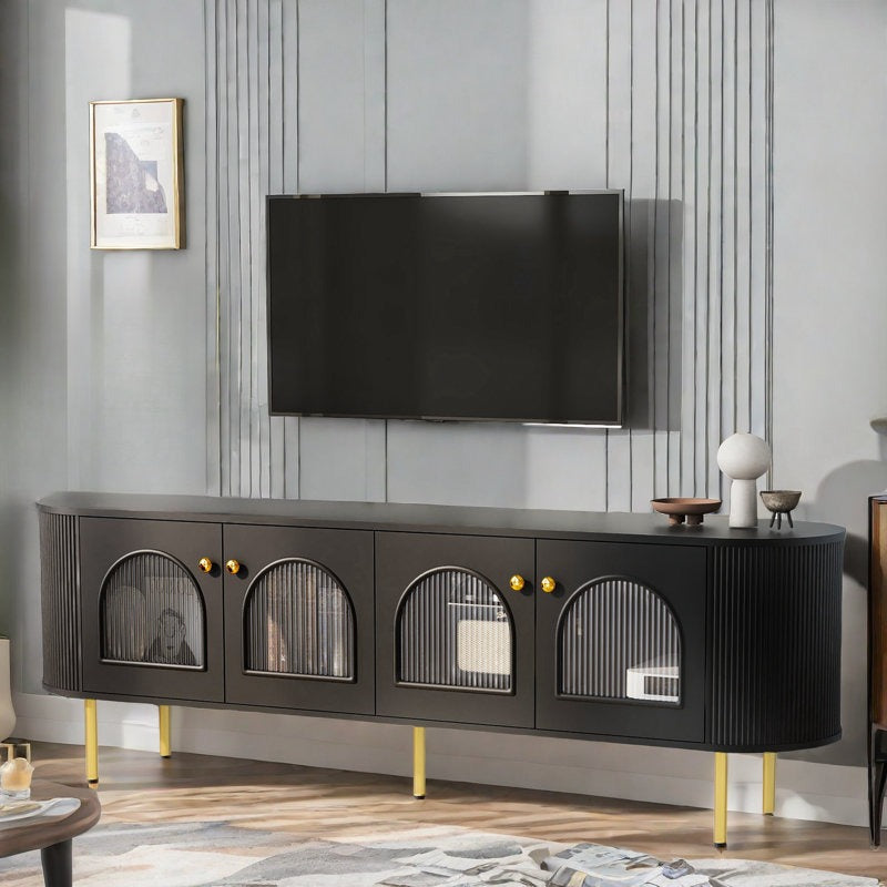 A black Mint TV stand with curved edges and fluted glass shutters, featuring golden handles and knobs, and standing on gold legs, with a flat-screen TV on top.