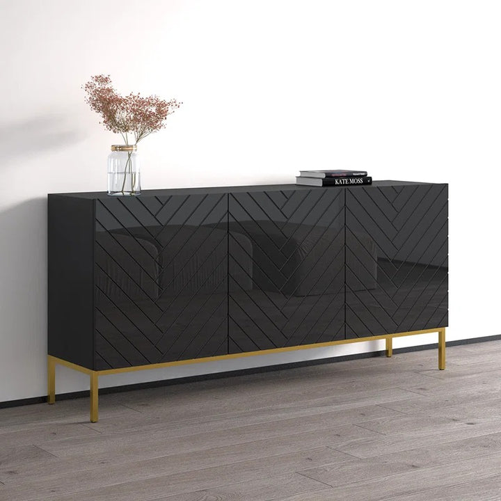 A modern black sideboard with geometric patterned panels, featuring gold-colored hardware and open shelves, set against a wall with a vase and books.