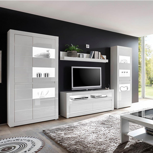 A modern white TV unit set with multiple drawers and open shelves, placed in a living room setting with a flat-screen TV on top, surrounded by a black wall, a white rug, and decorative items.
