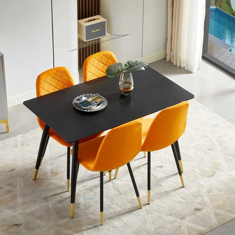 A modern dining table with four chairs upholstered in orange fabric, featuring black metal legs with gold coating accents.