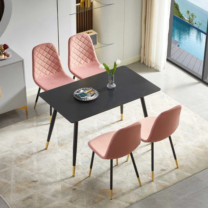A set of four pink upholstered dining chairs with black metal legs around a square dining table, placed on a rug in a room with a pool view.