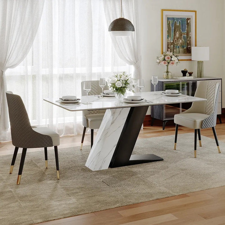 An 8-seater dining table set with a combination of white marble top and black PU paint finish dual-leg design, accompanied by chairs with a metal frame and leatherette upholstery, set in a modern dining room.