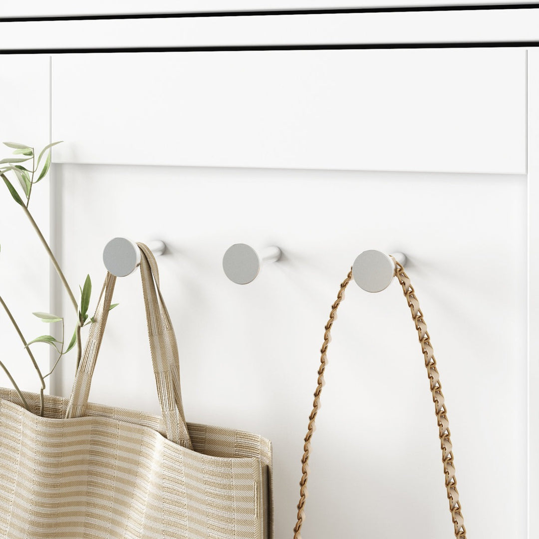 Three silver hooks on a white modular wardrobe with a woven bag and a rope hanging from one of them.