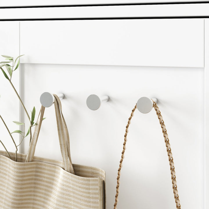 Three silver hooks on a white modular wardrobe with a woven bag and a rope hanging from one of them.