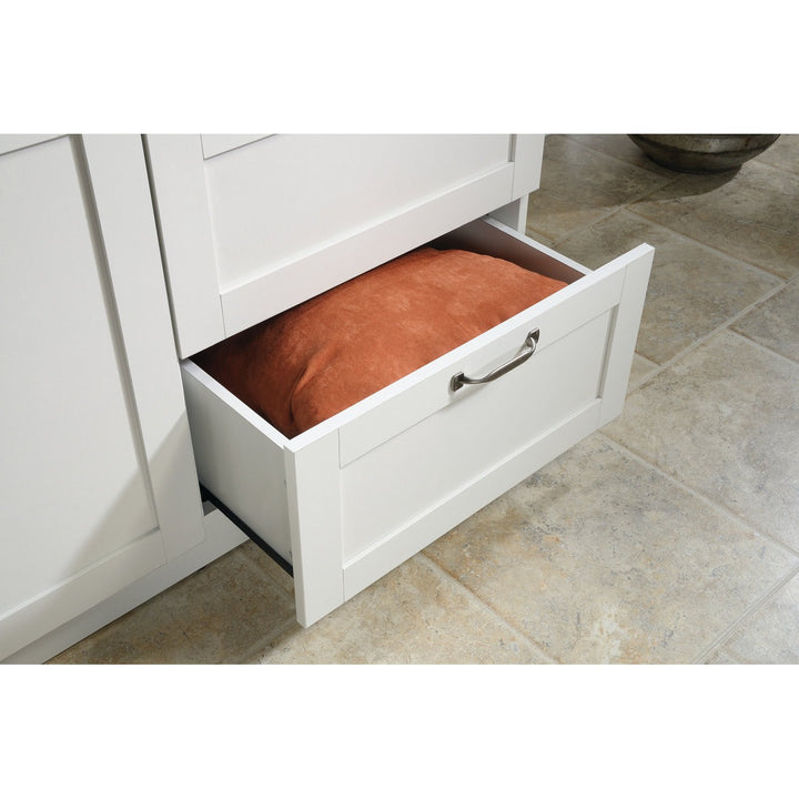 White cabinet with an open drawer containing a brown cushion on a tiled floor.