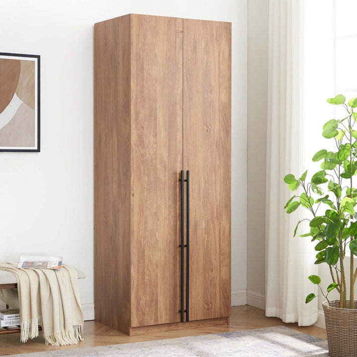 A 2-door wardrobe in beech wood finish with long vertical handles and a matte textured surface, placed in a room with a plant and a picture frame on either side.