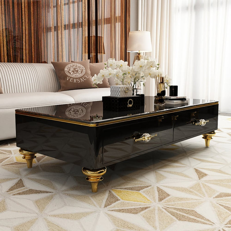 A luxurious black coffee table with a marble top, gold trim, and four drawers, placed on a patterned floor in a living room setting.