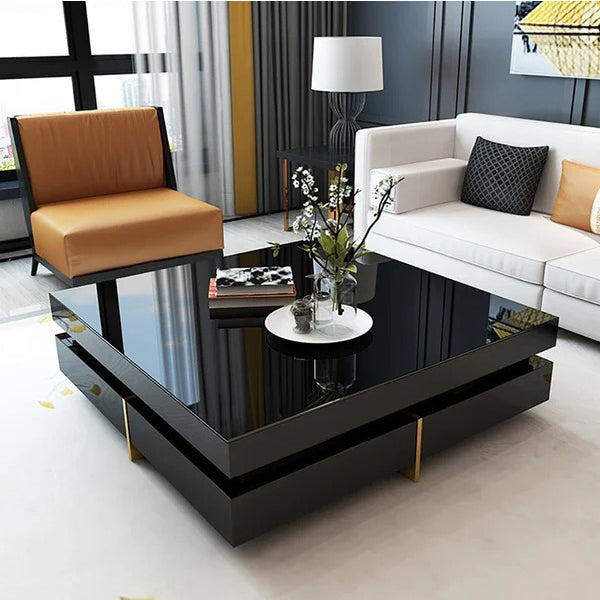 A black Nadu Coffee Table with metal golden legs, placed on a white carpet in a stylishly decorated living room.