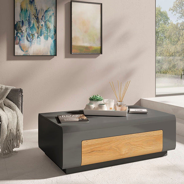 premium black coffee table with a wooden drawer, placed in a bright living area with abstract art hanging on the wall, a plant, and a magazine selection.
