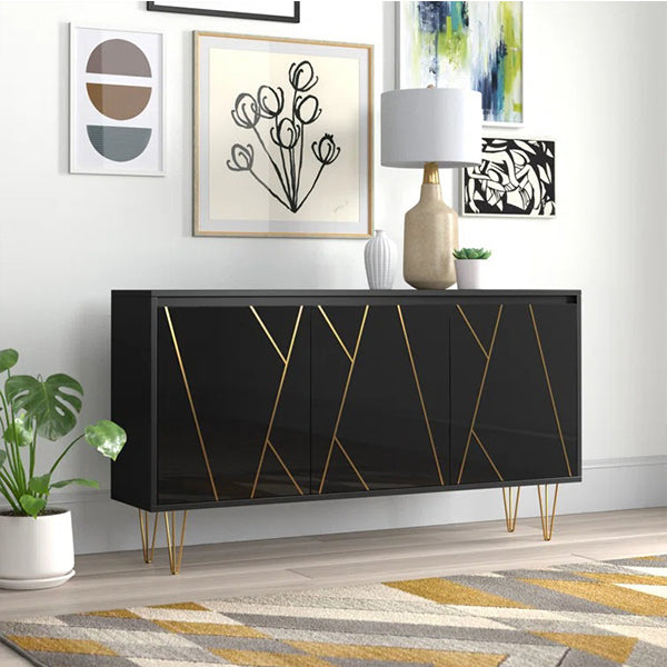 A black sideboard with golden hairpin legs and asymmetric golden door designs, placed in a room with decorative items and a plant beside it.