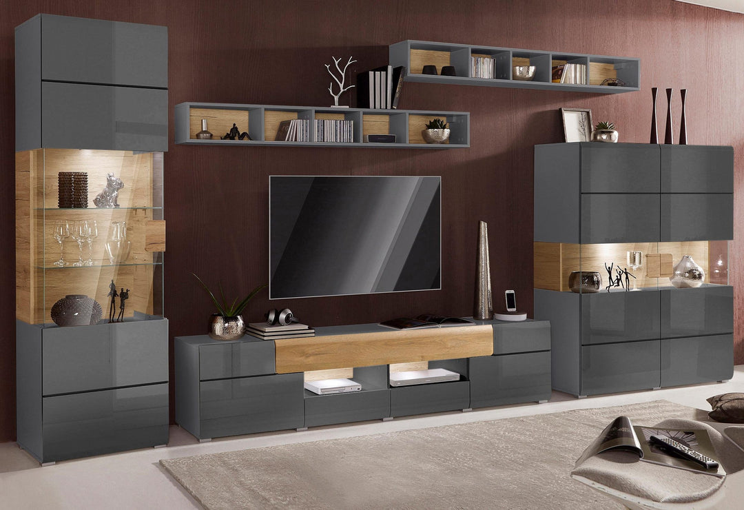A modern black TV unit set with a black PU paint finish, featuring open shelves, drawers, and a flat-screen TV, placed in a room with a wooden wall panel and a variety of decorations.
