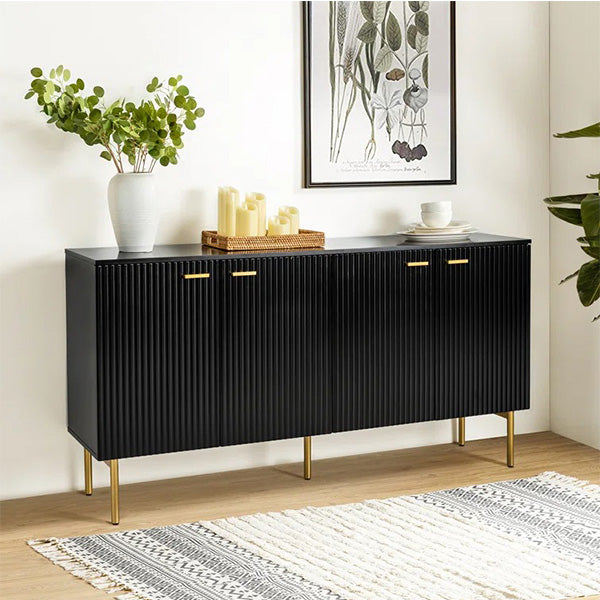 A large black sideboard with vertical lines and gold accents, featuring four cabinet doors and a metal handle, placed in a room with a decorative items on top.
