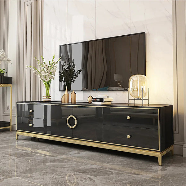 A black TV stand with golden accents, featuring a flat rectangular top and a frontal design with a golden finish. The stand is positioned in a room with a marble floor and a decorative lamp on top.