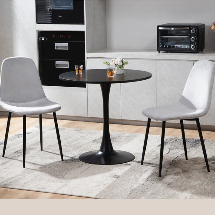 A modern dining table set with two chairs in a monochromatic color scheme, featuring a round tabletop and black metal legs on a grey area rug. The chairs have white upholstered fabric seats and backs.