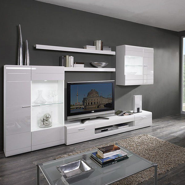 A white Dak TV unit set with glass doors, open shelves, and drawers, placed in a room with a flat-screen TV, books, and decorative items.