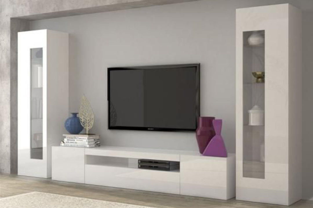 A white matte TV unit set with a flat-screen TV, magazines, and decorative items on top in a modern living room setting.