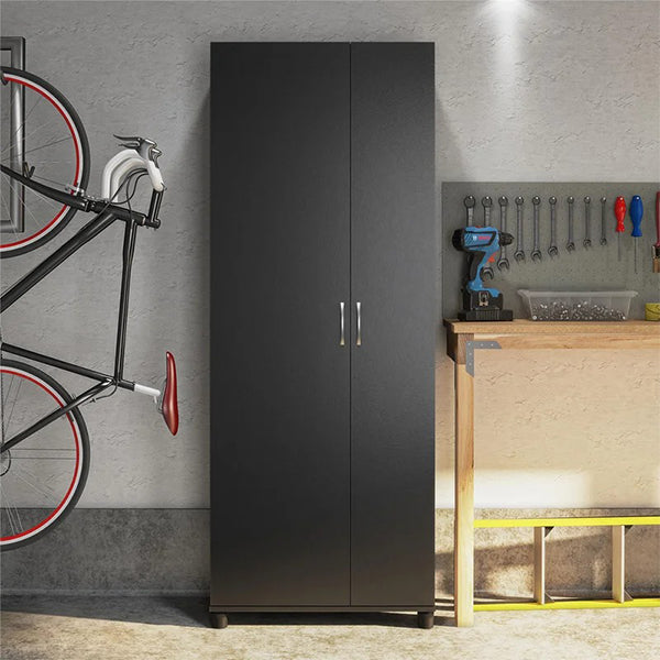 A black two-door wardrobe with silver metal handles, positioned against a wall next to a bicycle and a workbench with tools.