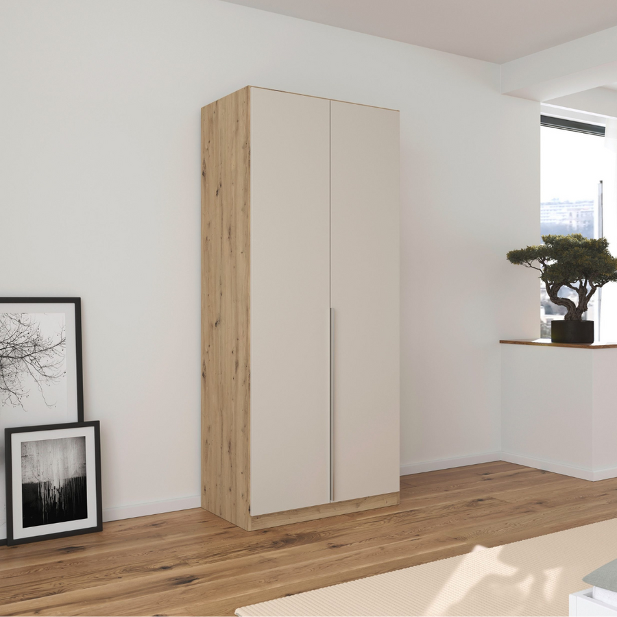 A 2-door wardrobe in a Beech/Beige finish with minimalistic handles, placed in a room with a framed picture and a bonsai tree on either side.
