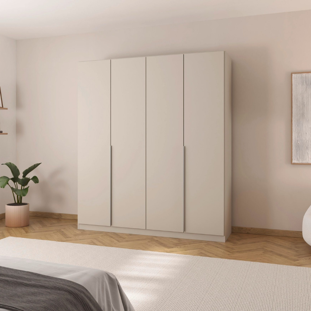 A beige 4-door wardrobe with handle-less design, placed in a bedroom setting with a visible plant and artwork on the walls.
