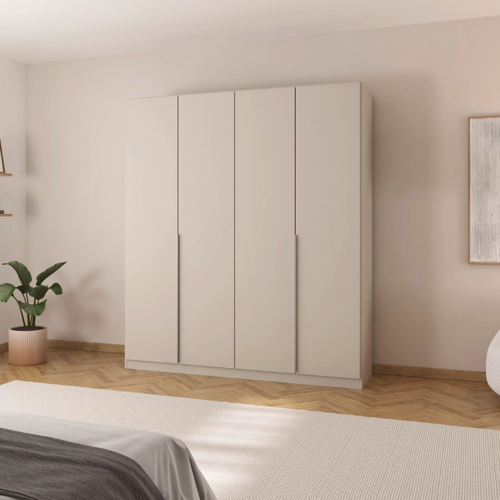 A beige 4-door wardrobe with handle-less design, placed in a bedroom setting with a visible plant and artwork on the walls.
