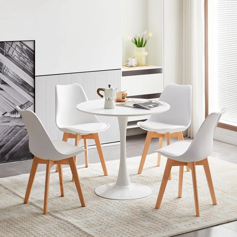 A modern white dining table with four chairs around it, set on a rug in a room with decorative items.