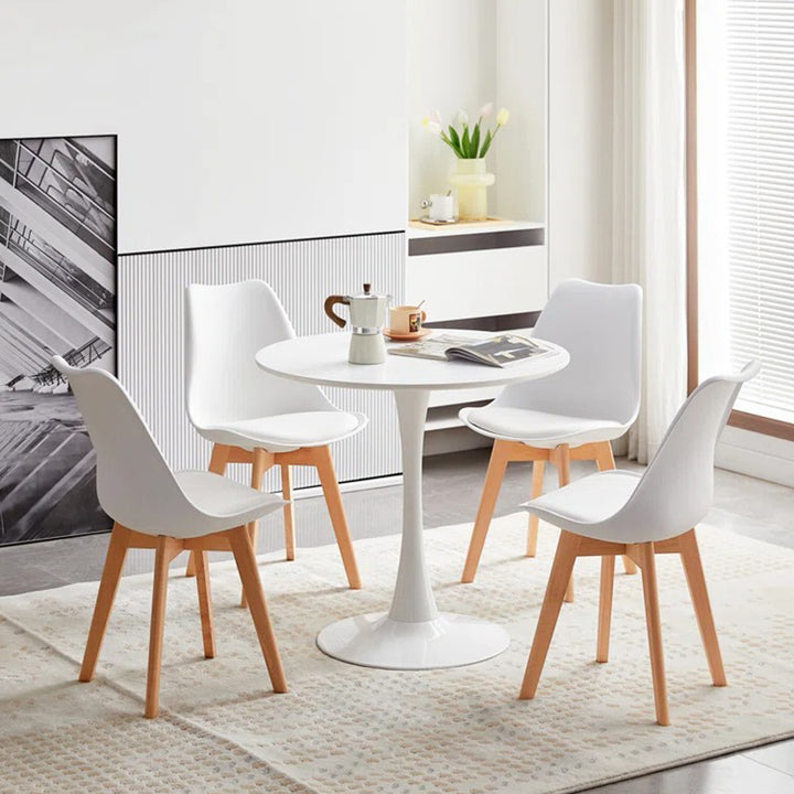 A modern white dining table with four chairs around it, set on a rug in a room with decorative items.