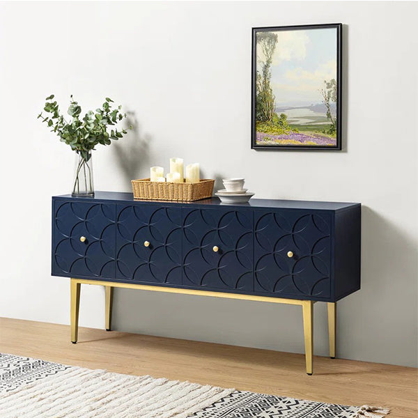 A navy blue sideboard with gold-colored legs and metal accents, featuring an intricate pattern on the front, placed against a wall with a framed picture and a wicker basket with candles.