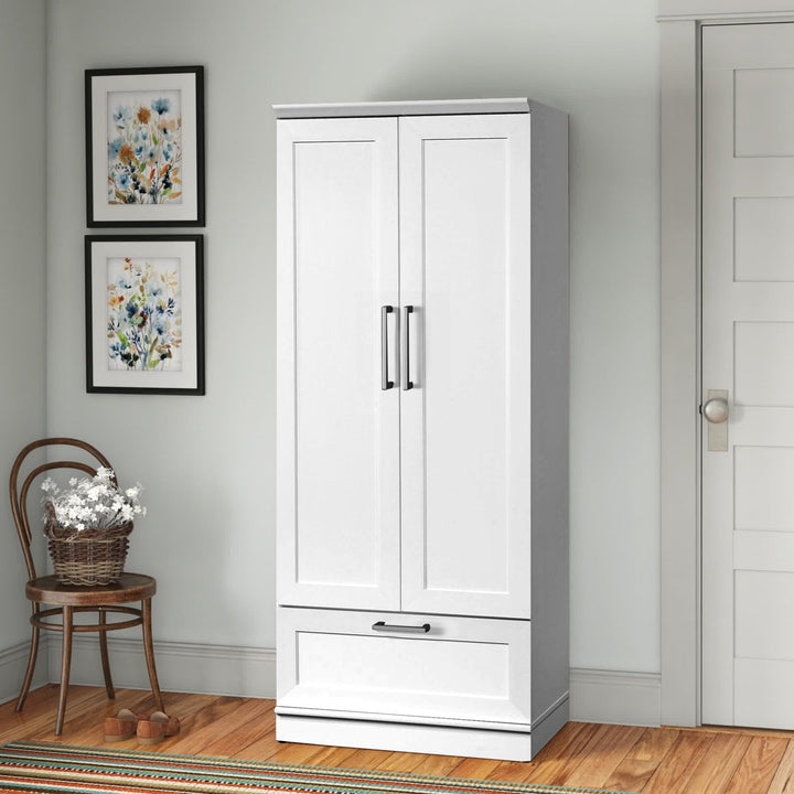 White wardrobe with two doors and a drawer in a room with wooden floor and framed artwork on the wall.