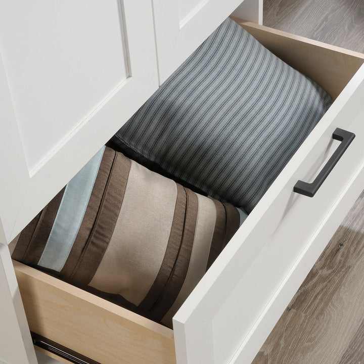 Open drawer with striped bed sheets inside, on a wooden floor.