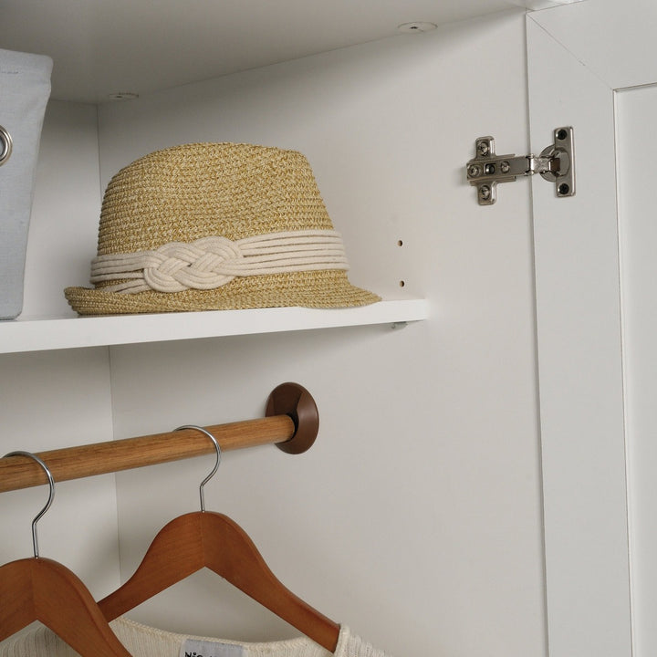 Straw hat on a shelf in a white closet with wooden hangers and a metal rod.