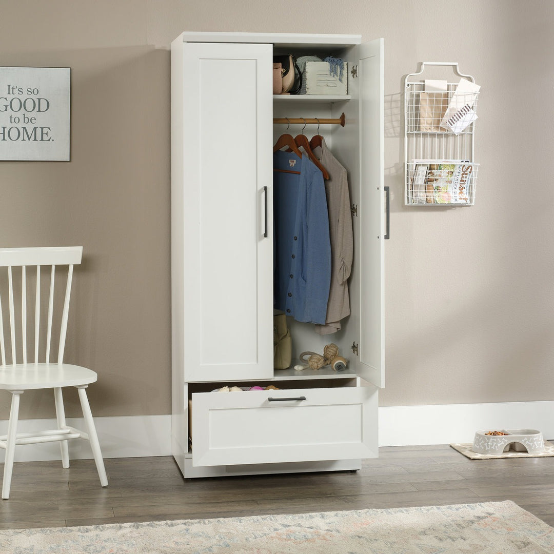 Stylish white wardrobe with clothes and shelves in a room with a chair and decorative items.