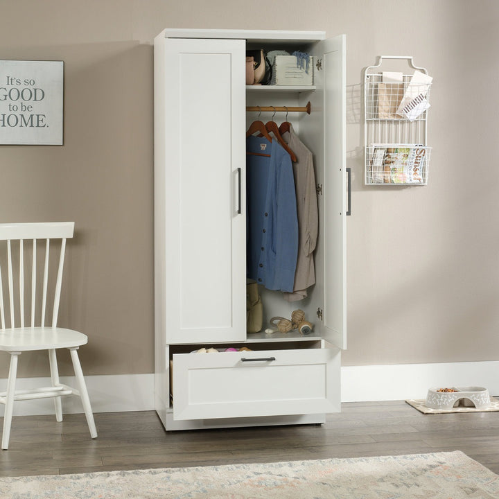 Stylish white wardrobe with clothes and shelves in a room with a chair and decorative items.