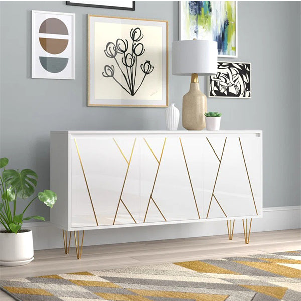 A white sideboard with golden hairpin legs and asymmetric door designs, featuring soft close operable shutters, placed in a room with decorations and a plant.