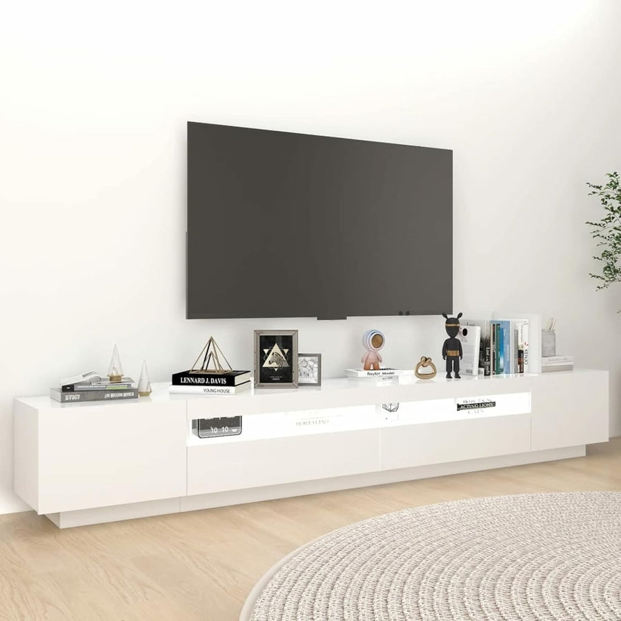 A white TV stand with multiple storage shutters and shelves, with a wall-mounted TV and various decorative items on top.