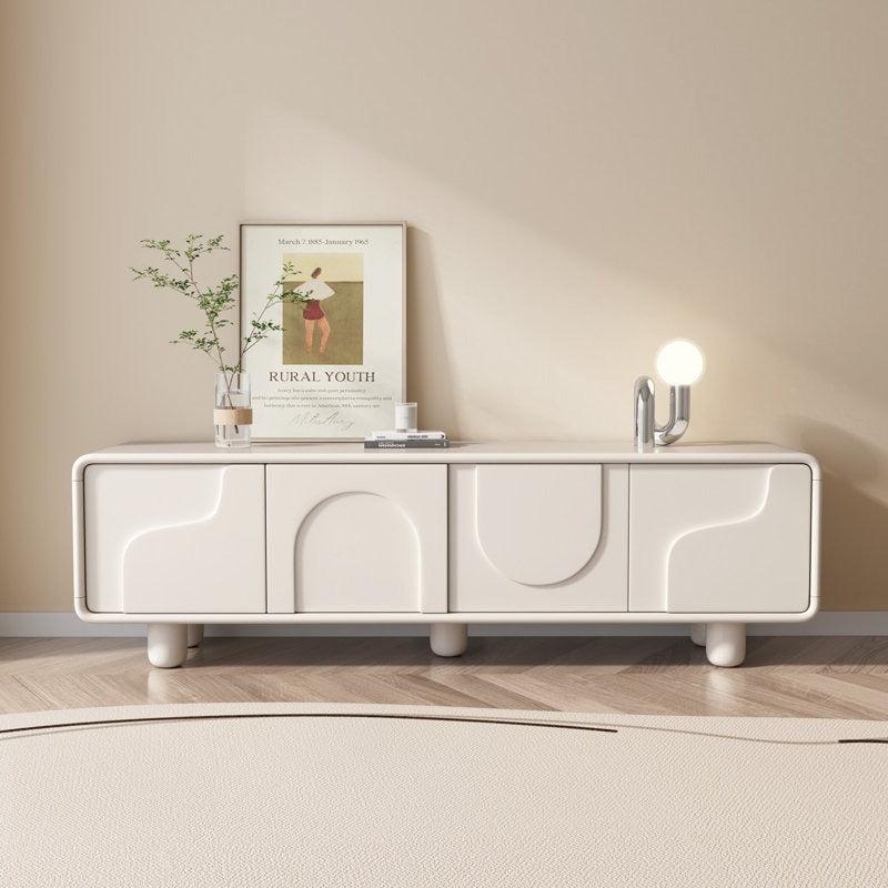 A large, white TV stand with a modern design, featuring four doors and a push-to-open mechanism. It is positioned in a minimalist-styled room with a framed picture and a lamp on top.