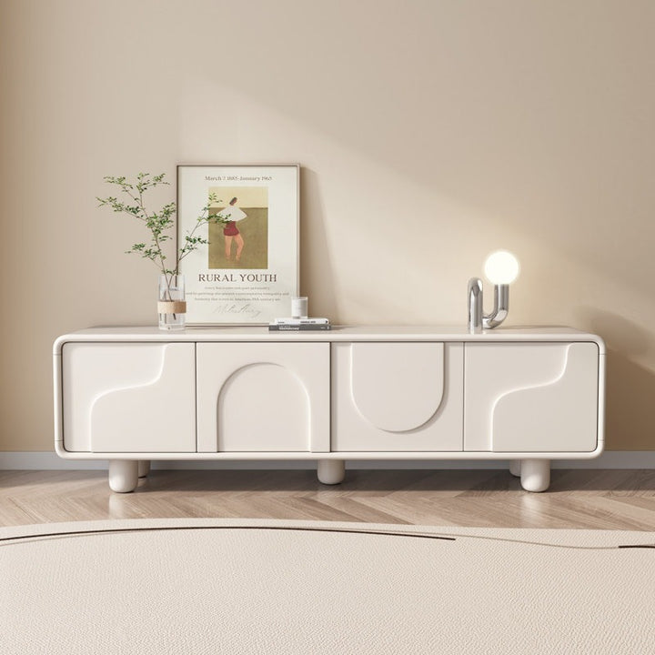 A large, white TV stand with a modern design, featuring four doors and a push-to-open mechanism. It is positioned in a minimalist-styled room with a framed picture and a lamp on top.