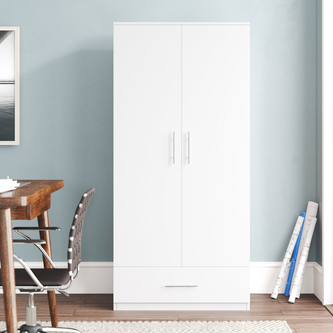 White wardrobe against a light blue wall with a wooden table and chair in the foreground.
