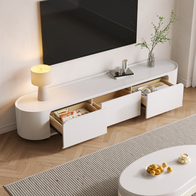 A modern white TV stand with curved edges, featuring ample storage with drawers and open shelves, placed in a room with a mounted TV on top and decorative items.