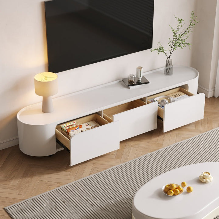 A modern white TV stand with curved edges, featuring ample storage with drawers and open shelves, placed in a room with a mounted TV on top and decorative items.