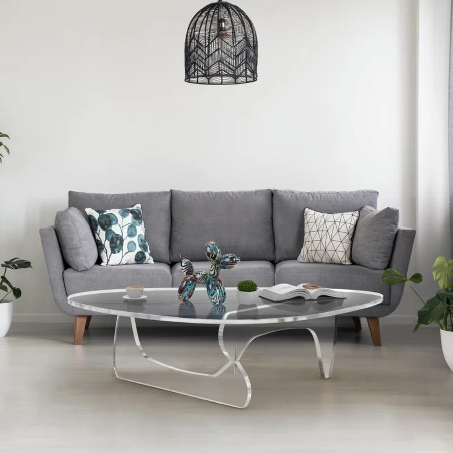 A clear acrylic coffee table with a geometric patterned rug on top in a living room setting.