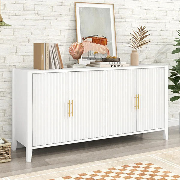 A small white sideboard with gold handles and a brushed finish, featuring two large openable shutters, placed in a room with decorative items on top.