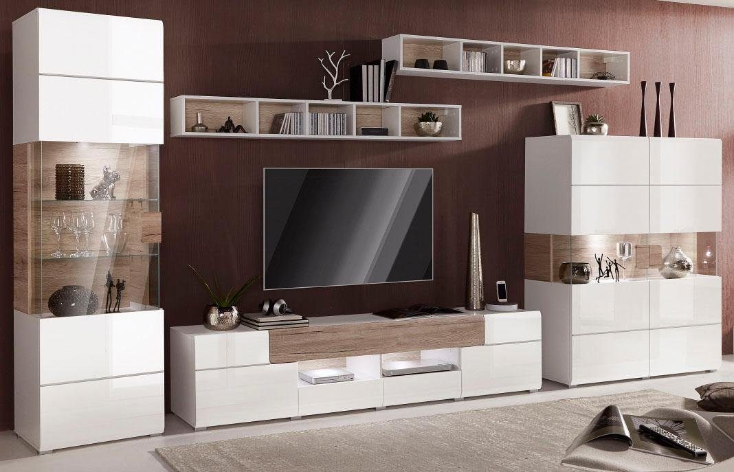 A modern white and beige TV unit set with glass doors, open shelves, and drawers, placed against a wall with an entertainment center and decorative items.