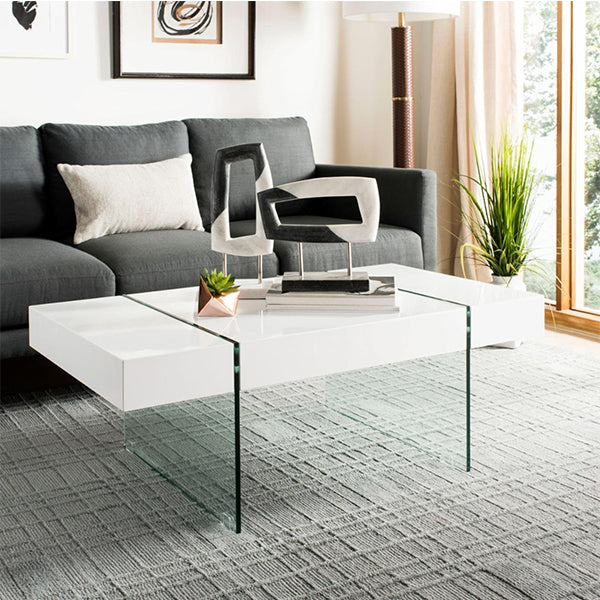 A white coffee table with glass legs on a rug in a modern living room setting, featuring a minimalist design.