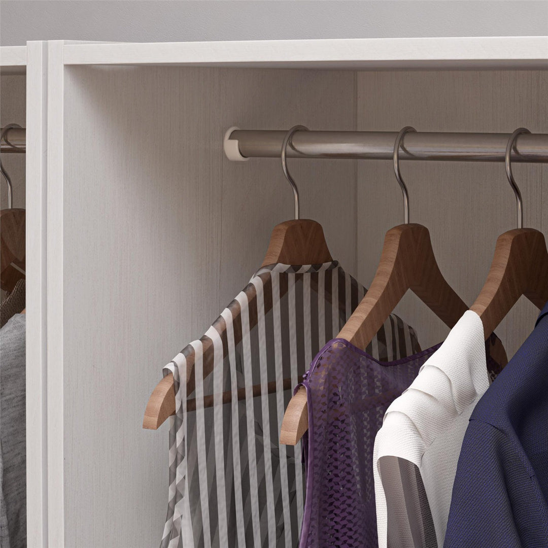 Clothing items on wooden hangers inside a white wardrobe.