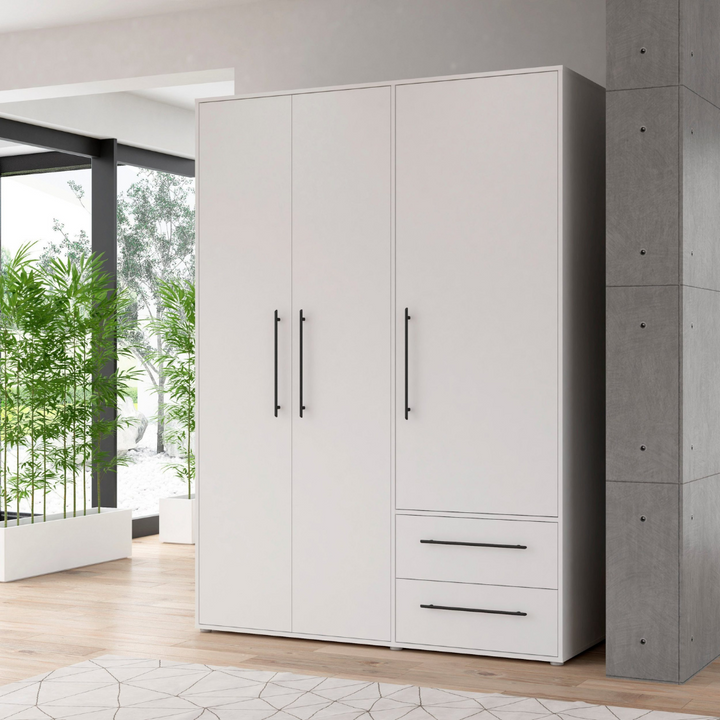 A modern white 3-door wardrobe with two drawers and multiple shelves in a room with concrete walls and wooden flooring.