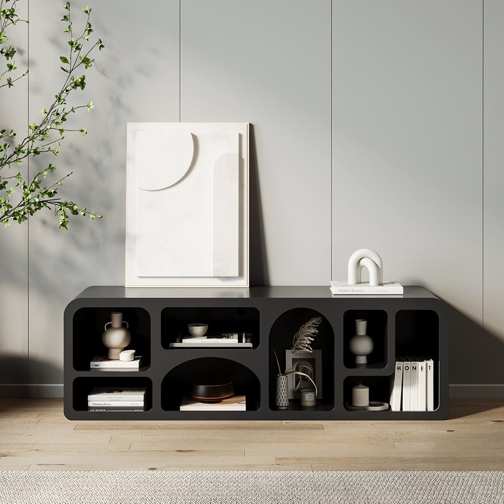 A modern black TV shelf unit with various items placed on it, set against a light-colored wall with a plant to the side.