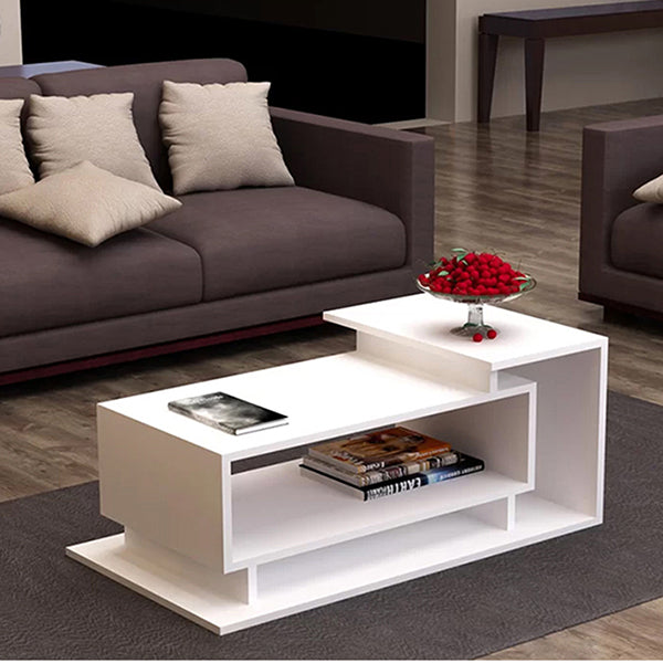 A white coffee table with a single shelf, placed on a grey area rug in a living room setting, with couches in the background and a vase with red flowers on top of the coffee table.